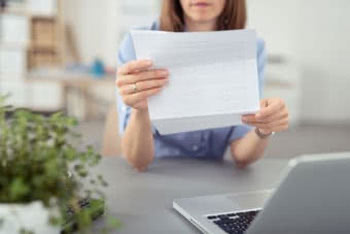 Frau liest in einem Schreiben im Vordergrund Laptop